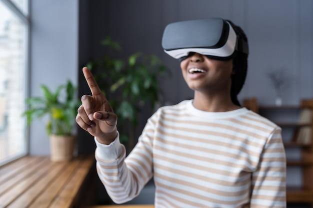 Chica negra con gafas de realidad virtual sintiéndose emocionada y asombrada tocando un objeto en el mundo virtual