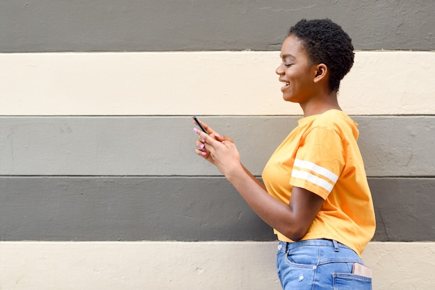 Chica negra sonriendo y usando su teléfono inteligente al aire libre.