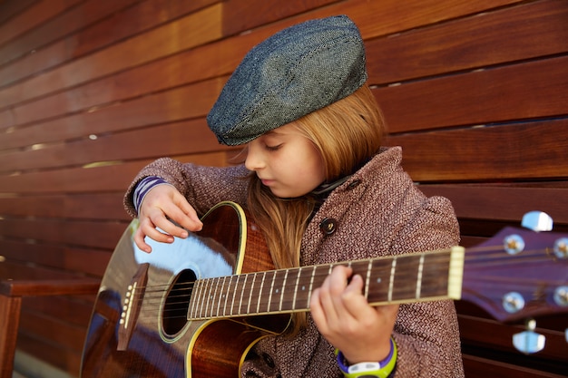 Chica de niño rubio tocando la guitarra con boina de invierno