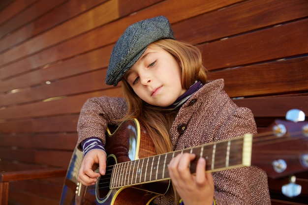 Chica de niño rubio tocando la guitarra con boina de invierno