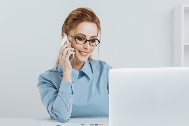 Chica de oficina bastante rubia hablando por teléfono en su lugar de trabajo.