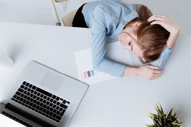 Chica de oficina joven sentada en su lugar de trabajo sintiéndose mal. La mujer tiene dolor de cabeza. Parece cansado.