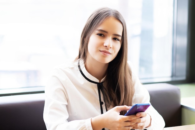 Chica oficinista en un café con un teléfono inteligente, sonriendo