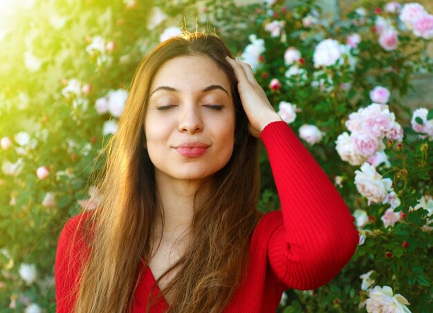 Chica con ojos cerrados entre rosas respira en primavera