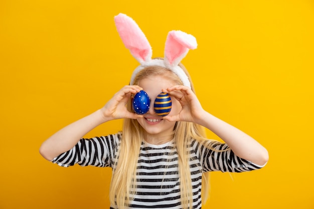 Chica en orejas de conejo en la cabeza con huevos de Pascua en los ojos en amarillo