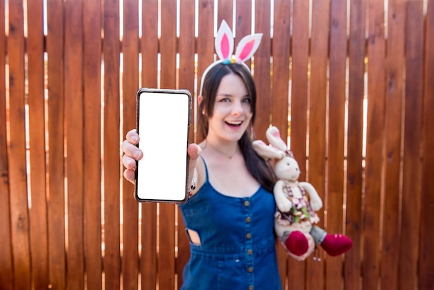 Chica con orejas de conejo con teléfono celular y enfoque selectivo de conejito de pascua