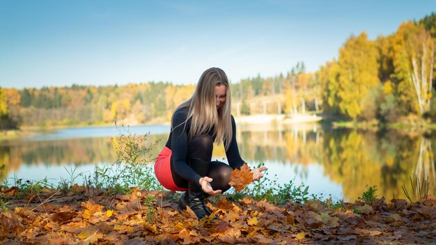 Chica en la orilla del embalse en otoño recoge hojas amarillas Concepto espacial