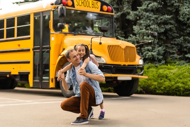 Chica con padre volviendo a la escuela cerca del autobús escolar