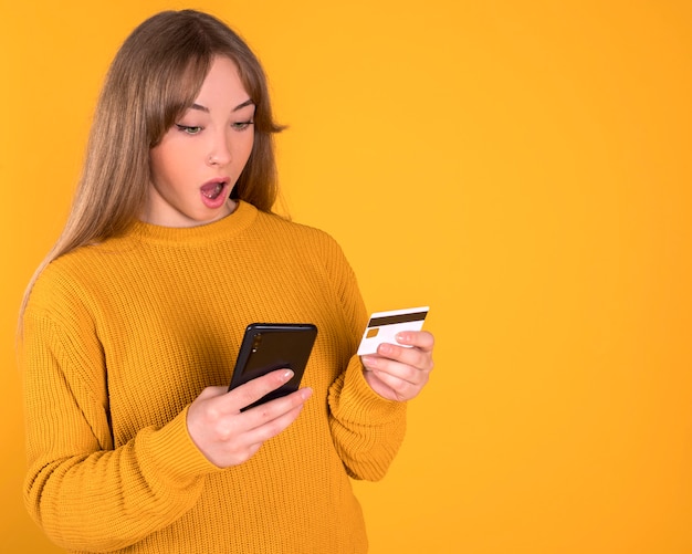 Chica pagando con tarjeta de crédito, cara sorprendida está comprando en línea desde su teléfono inteligente