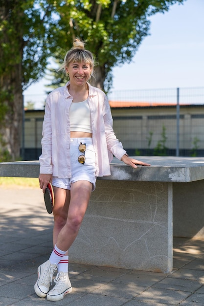 una chica con pantalones cortos se para cerca de la mesa con raquetas de tenis de mesa en las manos