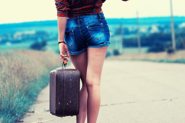 Chica en pantalones cortos con una maleta en la carretera