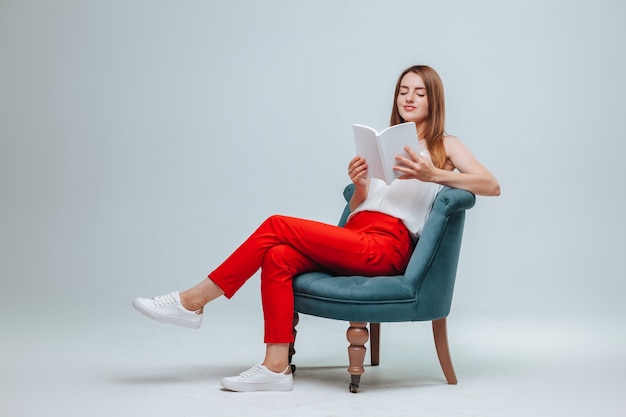 Chica en pantalones rojos sentada en una silla sobre un fondo gris claro