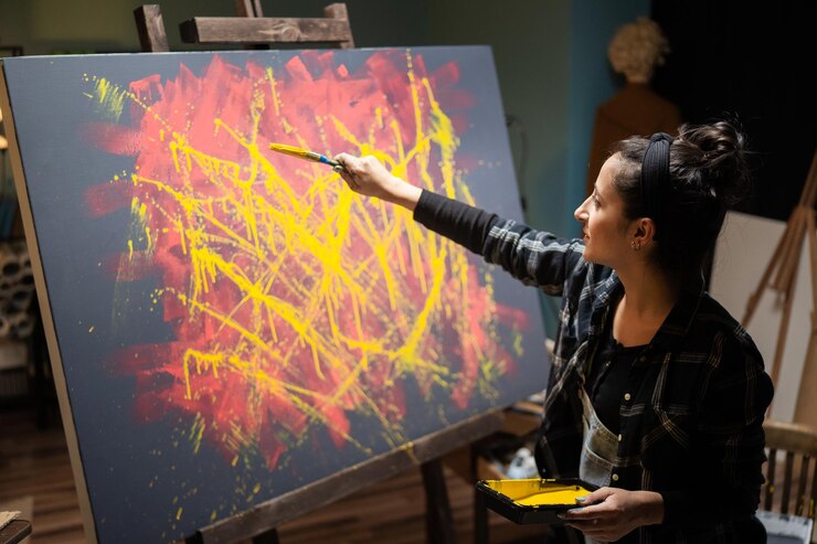 La chica pasa tiempo en el estudio pintando un cuadro abstracto en tonos amarillos y rojos.