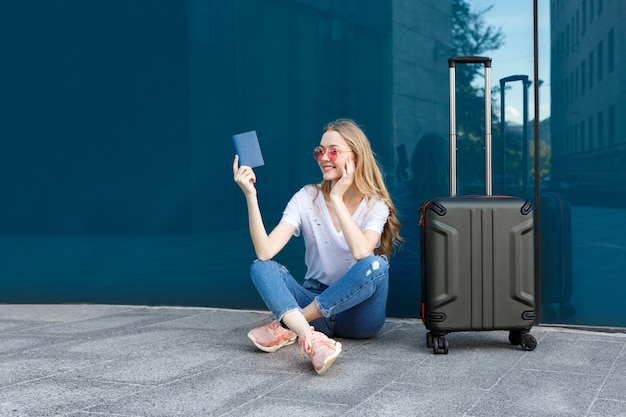 Chica con pasaporte, equipaje y gafas cerca de la ventana.