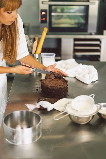 Chica pastelera está preparando un bizcocho con crema blanca y tortas de chocolate para cocinar