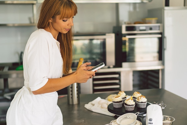 Chica pastelera fotografiando cupcakes para su blog chica hace una foto de cupcakes en un teléfono inteligente