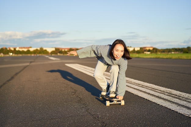 Foto chica patinadora despreocupada en su patineta montando longboard en una carretera vacía cogidos de la mano de lado y