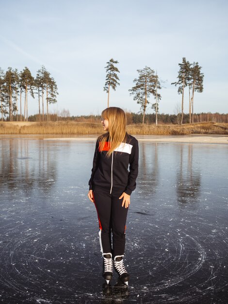 Chica patinando sobre el hielo de un lago del bosque