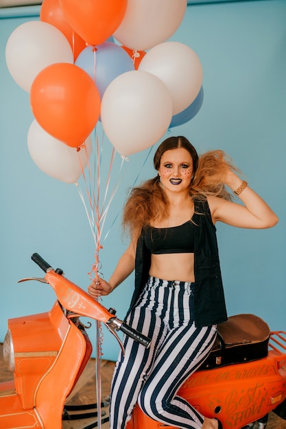 Chica de payaso de moda joven posando en moto