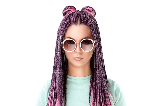 Chica con peinado de trenzas rosa en ropa turquesa y gafas de sol aislar sobre un fondo blanco. Concepto de estilo moderno, inclusión, espacio de copia.