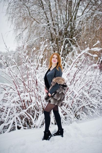 Chica pelirroja con abrigo de piel caminando en el parque nevado de invierno