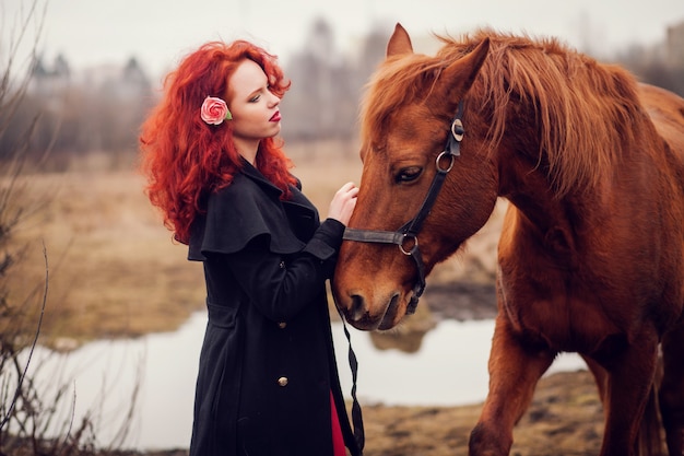 Chica pelirroja acariciando el caballo.