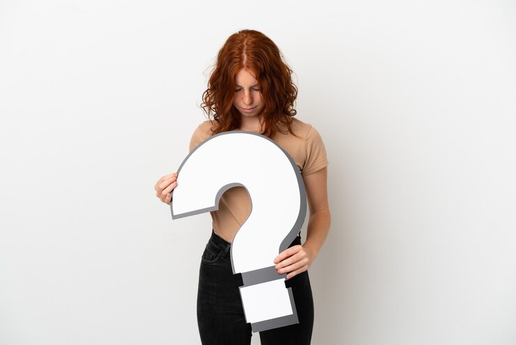 Foto chica pelirroja adolescente aislada sobre fondo blanco sosteniendo un icono de signo de interrogación