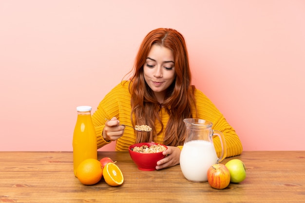 Chica pelirroja adolescente desayunando en una mesa