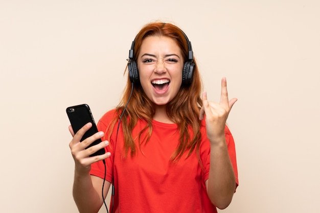 Chica pelirroja adolescente escuchando música y haciendo gesto de rock