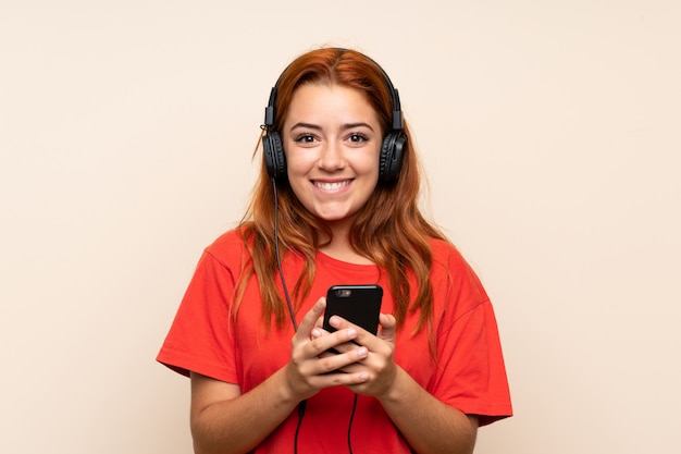 Chica pelirroja adolescente escuchando música con un móvil sobre aislado