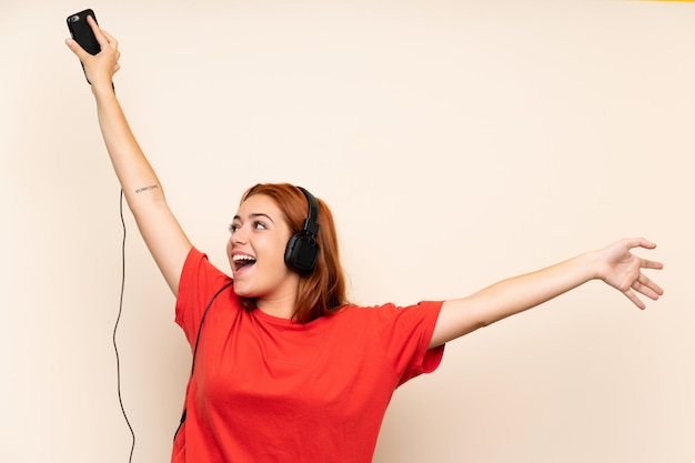 Chica pelirroja adolescente escuchando música con un móvil