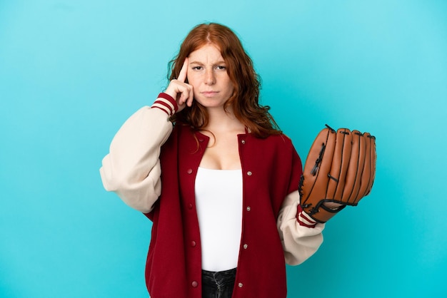 Chica pelirroja adolescente con guante de béisbol aislado sobre fondo azul pensando en una idea