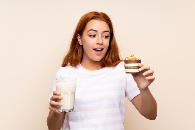 Chica pelirroja adolescente sosteniendo un vaso de leche y un panecillo