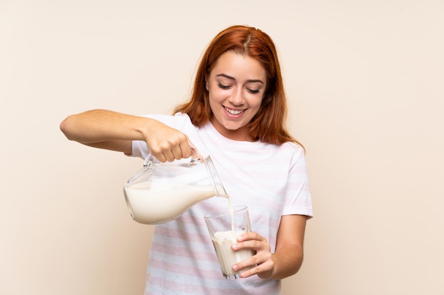 Foto chica pelirroja adolescente sosteniendo un vaso de leche sobre fondo aislado