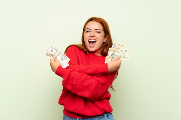Chica pelirroja adolescente con suéter sobre verde aislado tomando mucho dinero