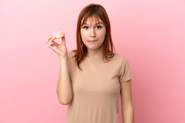 Chica pelirroja aislada sobre fondo rosa sosteniendo una rosquilla