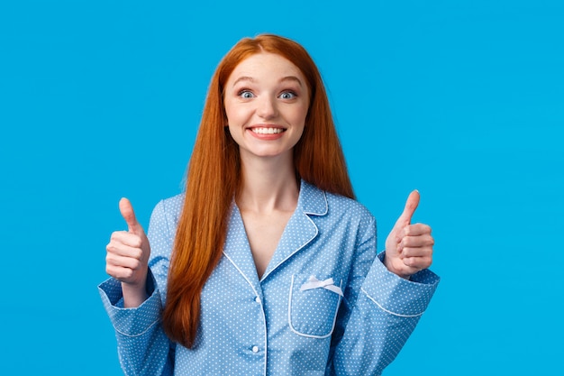 La chica pelirroja alegre y emocionada no puede esperar para probar, de acuerdo con la tentación y el interés, mostrando el pulgar hacia arriba sonriendo con entusiasmo y entusiasmo con aprobación, como idea, como una pared azul