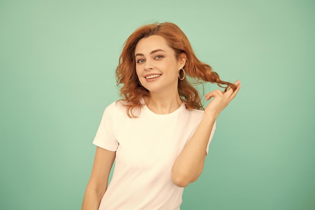 Chica pelirroja alegre con el pelo rizado sobre fondo azul.