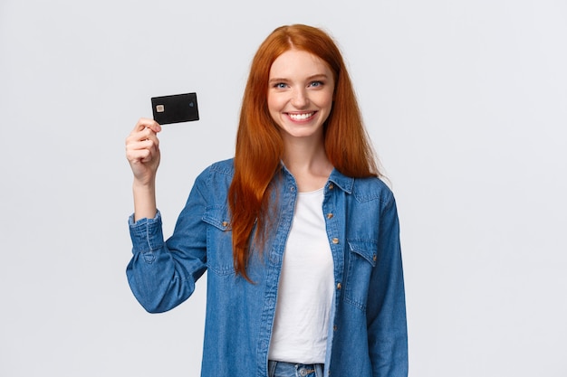 Chica pelirroja alegre con tarjeta de crédito y sonriendo