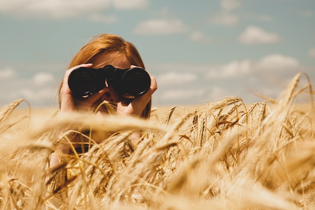 Chica pelirroja con binocular en el campo de trigo