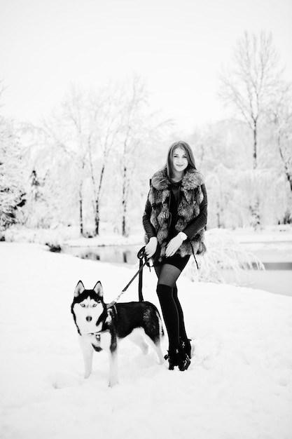 Chica pelirroja caminando en el parque con perro husky en día de invierno