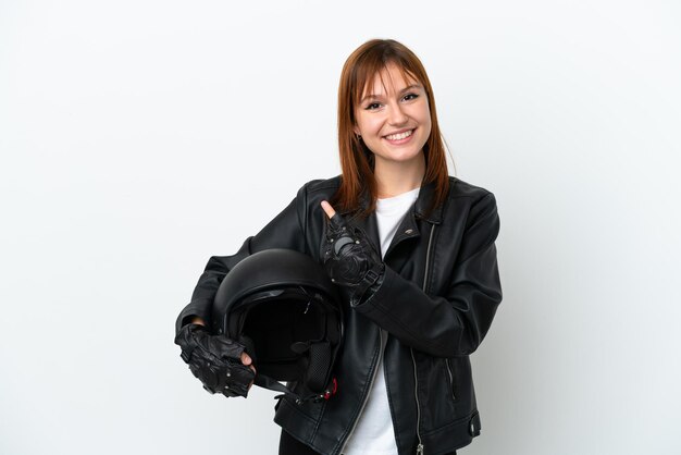 Chica pelirroja con casco de motocicleta aislado en fondo blanco apuntando hacia un lado para presentar un producto