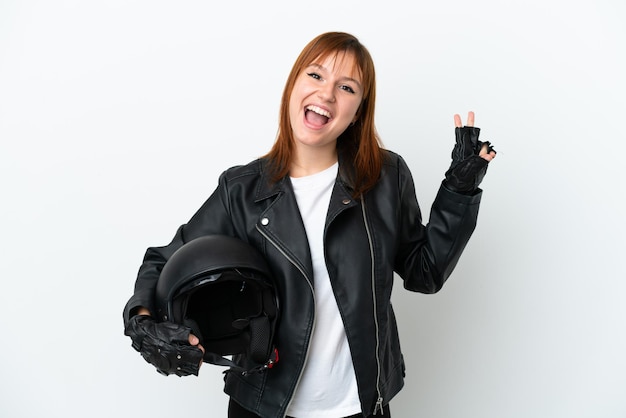 Chica pelirroja con un casco de motocicleta aislado sobre fondo blanco sonriendo y mostrando el signo de la victoria