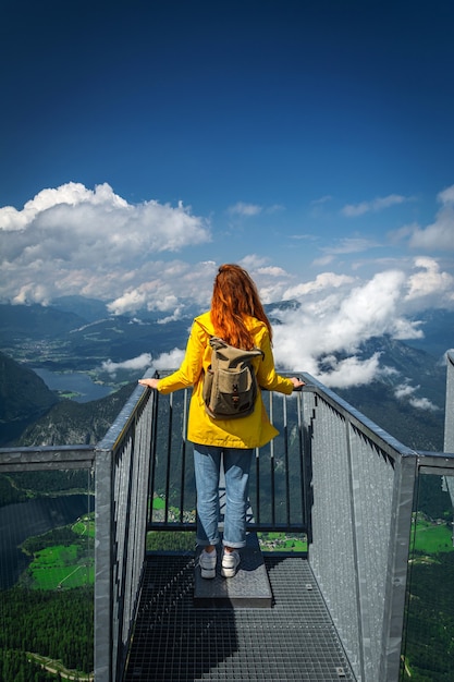 Foto chica pelirroja de chaqueta amarilla está mirando el lago hallstatter hallstatt y las montañas circundantes