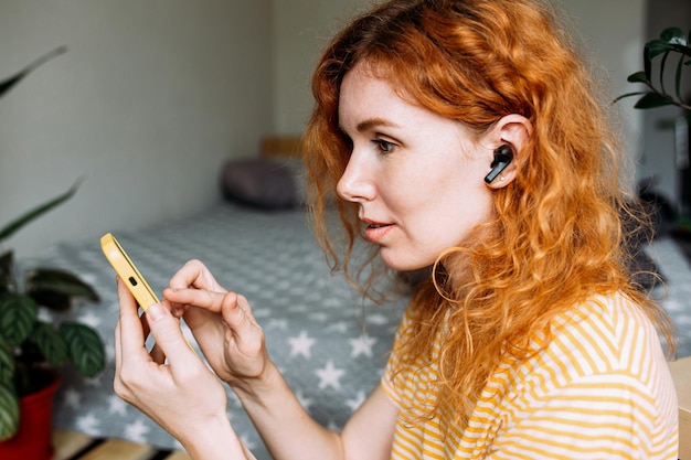 Chica pelirroja feliz escuchando música en casa con auriculares inalámbricos