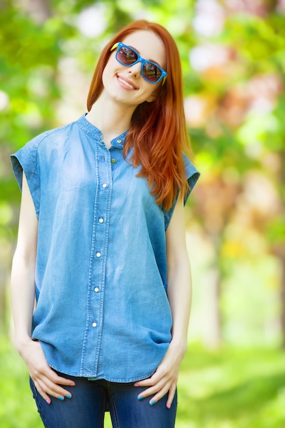 Chica pelirroja con gafas de sol en el parque en primavera.