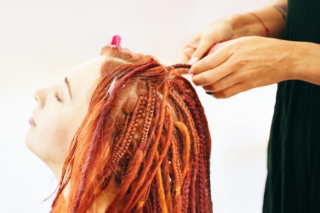 Chica pelirroja hace trenzas rastas rastas de kanekalon peinado de moda genial hecho de artif...