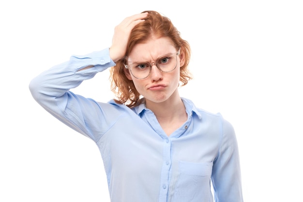 Chica pelirroja inteligente con camisa de negocios y anteojos toca la cabeza piensa que las dudas toman una decisión aislada en el fondo del estudio blanco