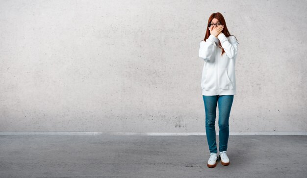 Chica pelirroja joven en una sudadera blanca urbana con gafas que cubren la boca