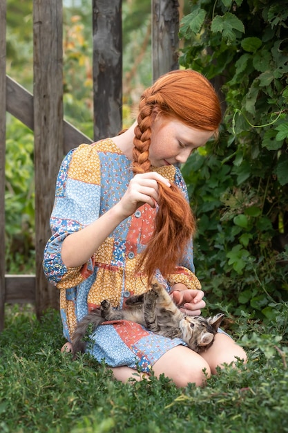 La chica pelirroja juega con un gatito en la calle en la hierba Chica de campo jugando con un gato